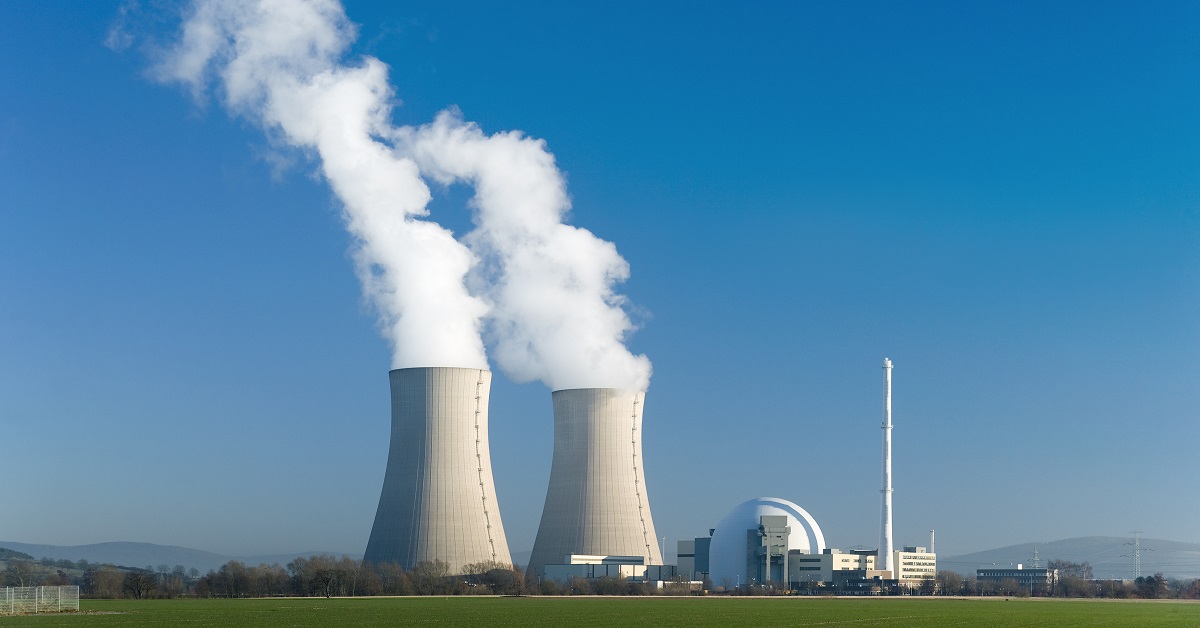 Nuclear power station with two steaming cooling towers in blue sky.
